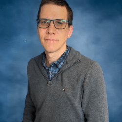 A middle-aged white man with rectangular glasses and close-cropped dark hair smiles mildly