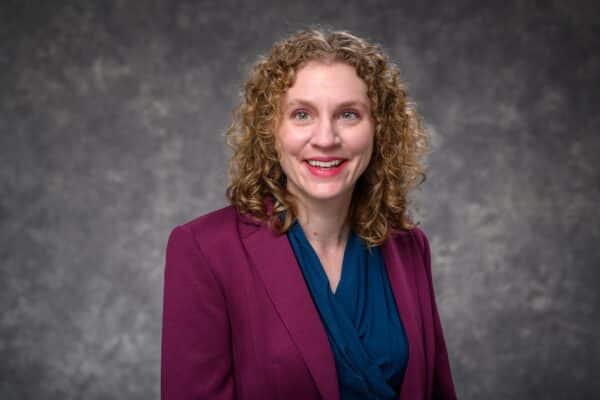 Steffi Diem: A white woman with blonde curly hair and a pink blazer smiling