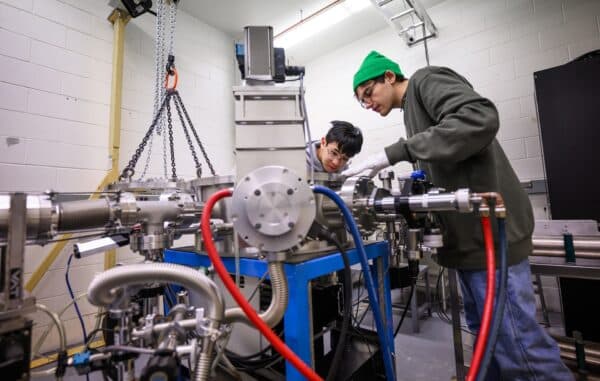 Two students hover over a particle accelerator that has been taken apart.